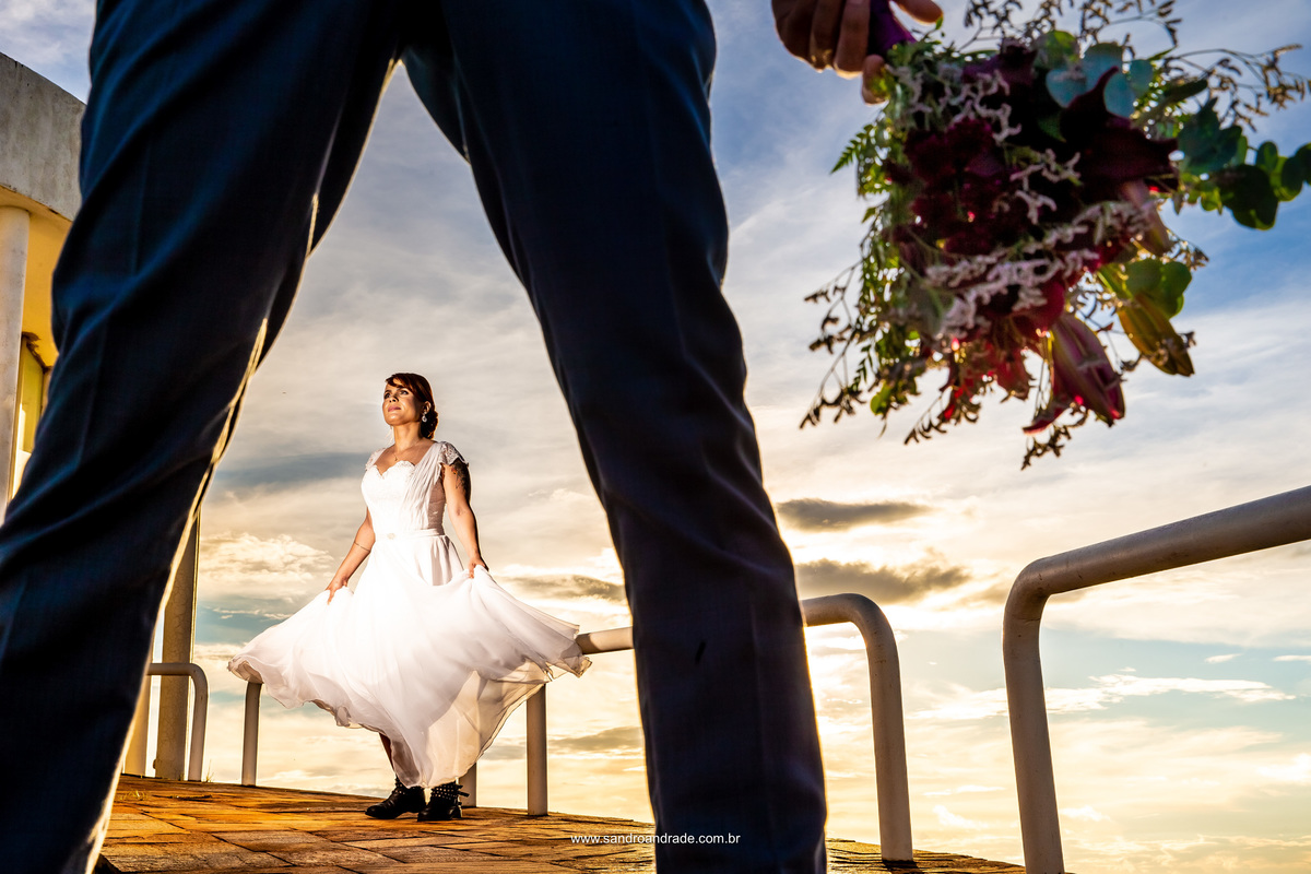 Nesta foto, aparece só as pernas do noivo, ele está com as pernas aberta, segurando o buque na lateral direita e a noiva entre as pernas dele, girando, movimentando seu lindo vestido. Fotografia é arte e nela o fotógrafo de casamento Sandro Andrade é top.