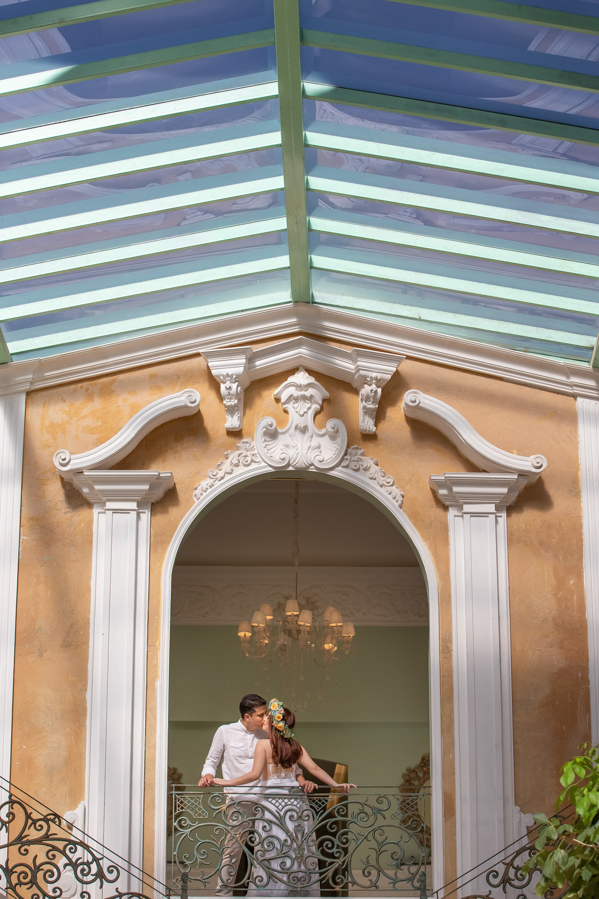 Na sequencia da foto anterior, agora pegando todo o ambiente, no topo da escadaria do palazzo, com o noivo dando um beijinho no rosto da noiva, em uma belíssima imagem colorida.