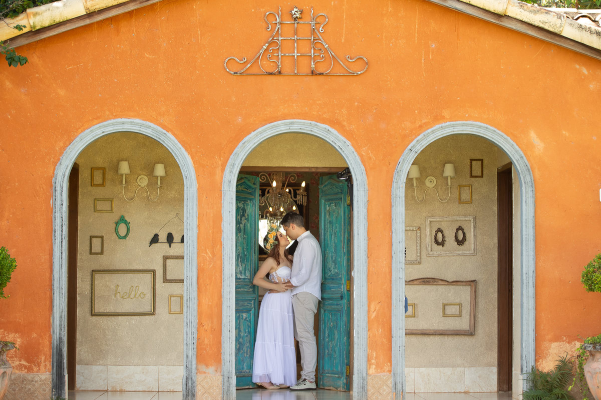 Se olhando ainda na porta, porem nesta fotografia colorida pega toda a frente do antigo quarto da noiva, o casal ao centro, muitas cores e o amor desse jovem casal contando os dias para seu grande dia.
