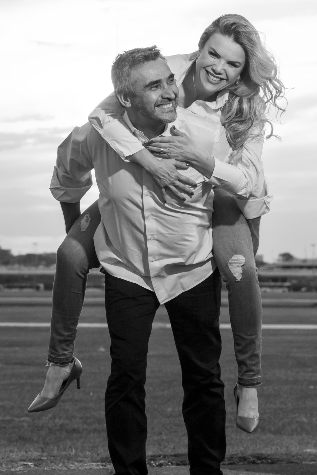 Brincando...Marcelo carregando Cris nas costas, ambos sorrindo e ele reclamando que está carregando ela (risos). Uma imagem preto e branco e o casal descontraídos.