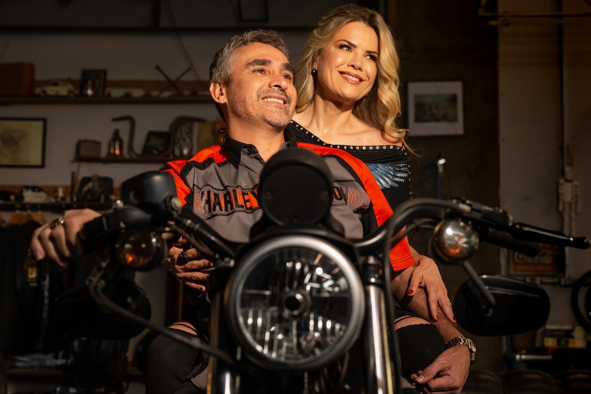 Neste retrato colorido, o Marcelo está com a mão no joelho da Cris e a outra no guidão da moto, ambos sorridentes e felizes.