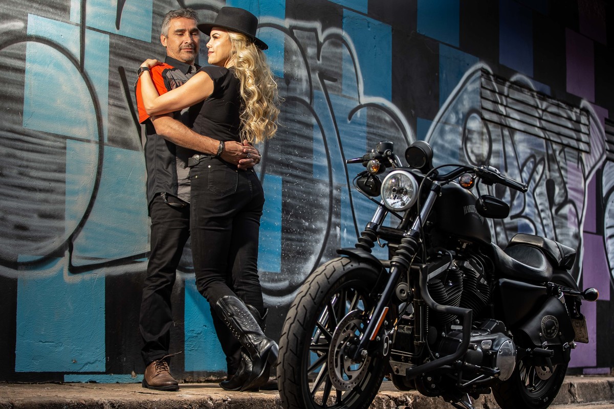 Eles estão namorando encostados na parede e a moto a frente.