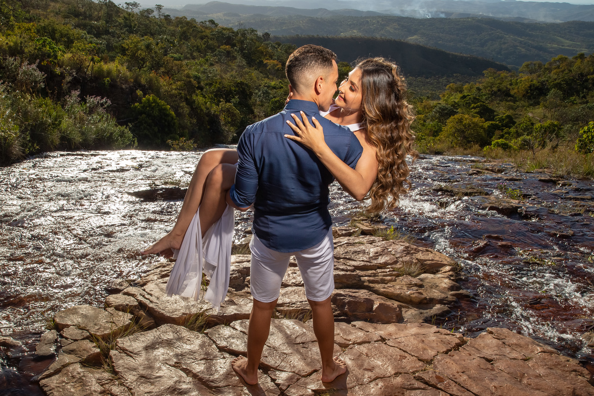 Linda fotografia com a cachoeira em composição e Ítalo está com sua linda noiva Dani no colo, felizes se olham apaixonados.