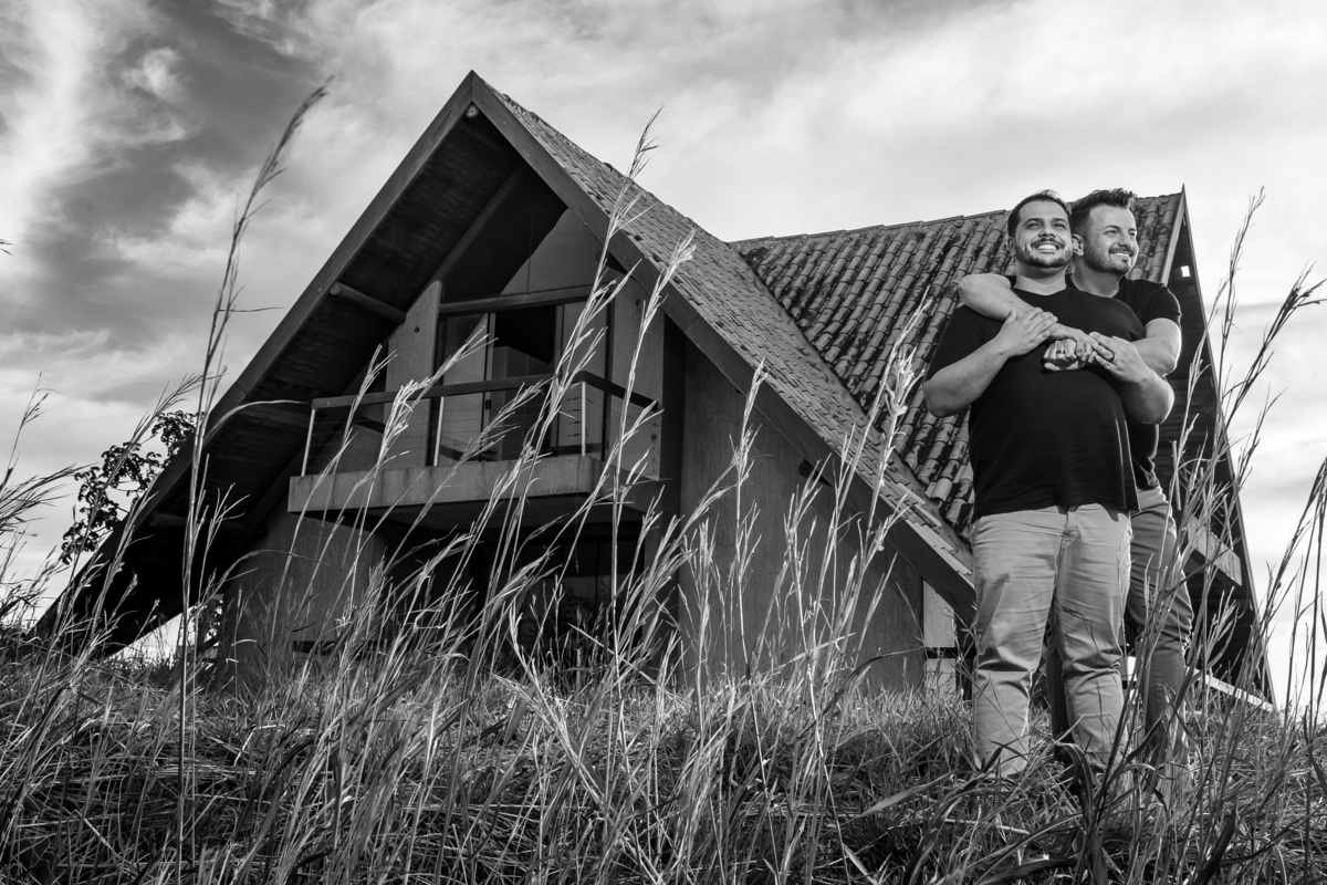 Ainda abraçados e muito felizes, eles estão brincando, rindo, aproveitando este momento especial em suas vidas com a casa de fundo e tudo preto e branco.