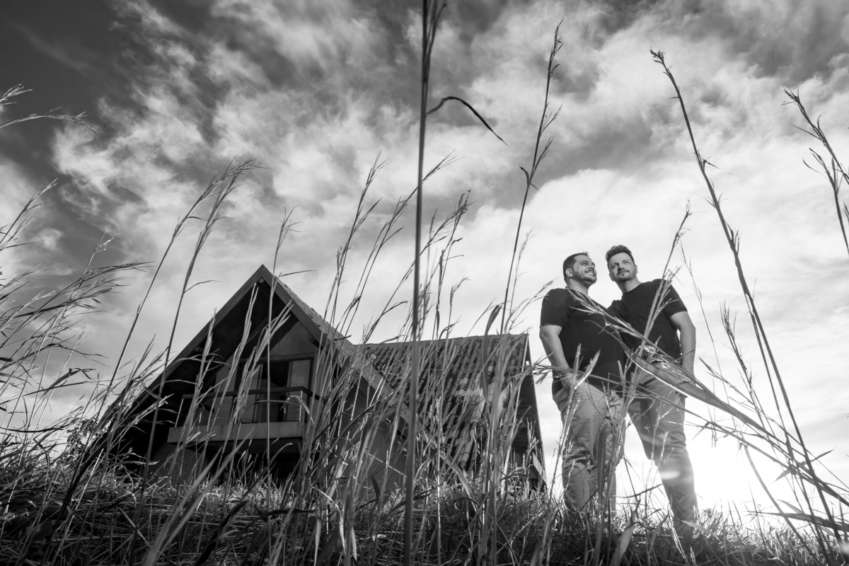 Os dois juntinhos no canto direito da foto em preto e branco, abraçados meio de lado um para o outro e uns matinhos em primeiro plano fazendo uma moldura no casal.