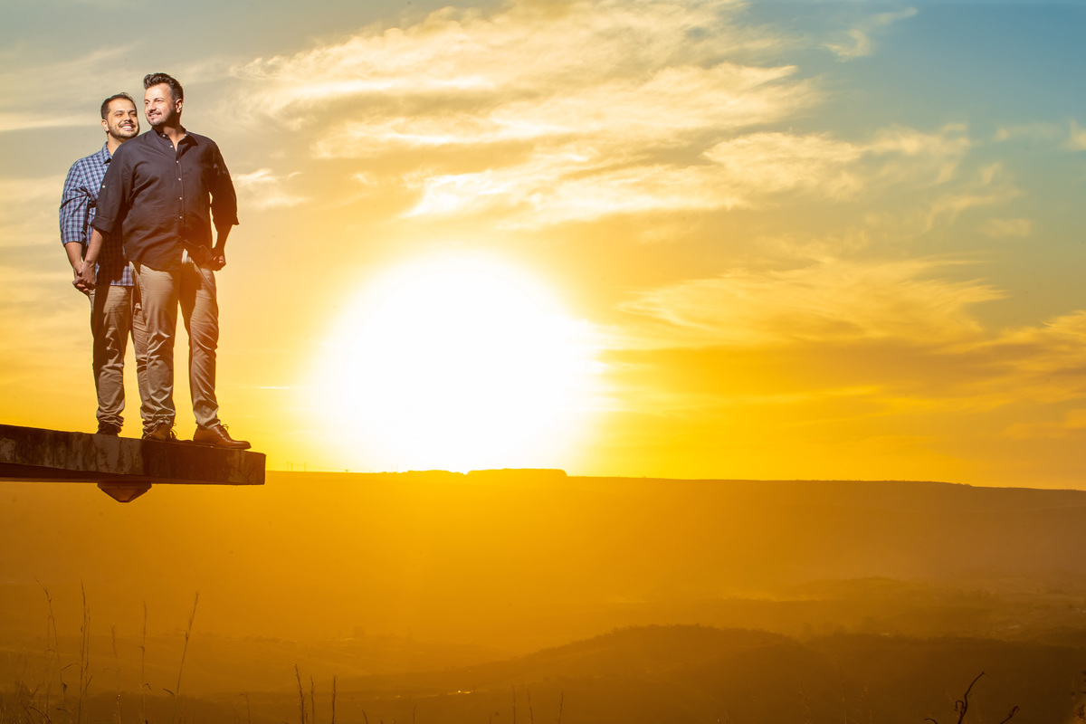 Meu DEUS...que pôr do sol, olha essa bola do sol no céu no horizonte, uau! O Jorge e o Victor estão em pé bem juntinhos, de mãos dadas, de corpo inteiro em uma linda fotografia colorida e com um toque maravilhoso do CRIADOR.