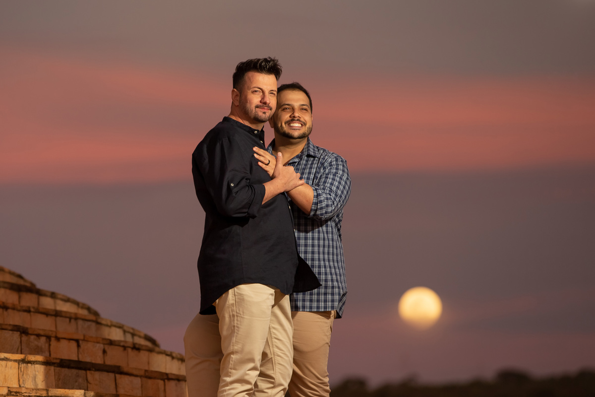 Abraçados eles posam na escadaria do templo com a linda lua nascendo ao fundo e o céu em tons de roxo, azul e laranja, muito lindo.