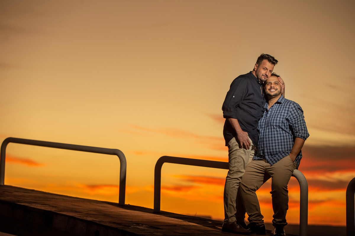 Que perfeição esta fotografia colorida, o sol já se pôs e o céu está maravilhoso em tons de amarelo e laranja, o Victor sentou no corrimão da rampa e o Jorge está ao lado dele o abraçando.