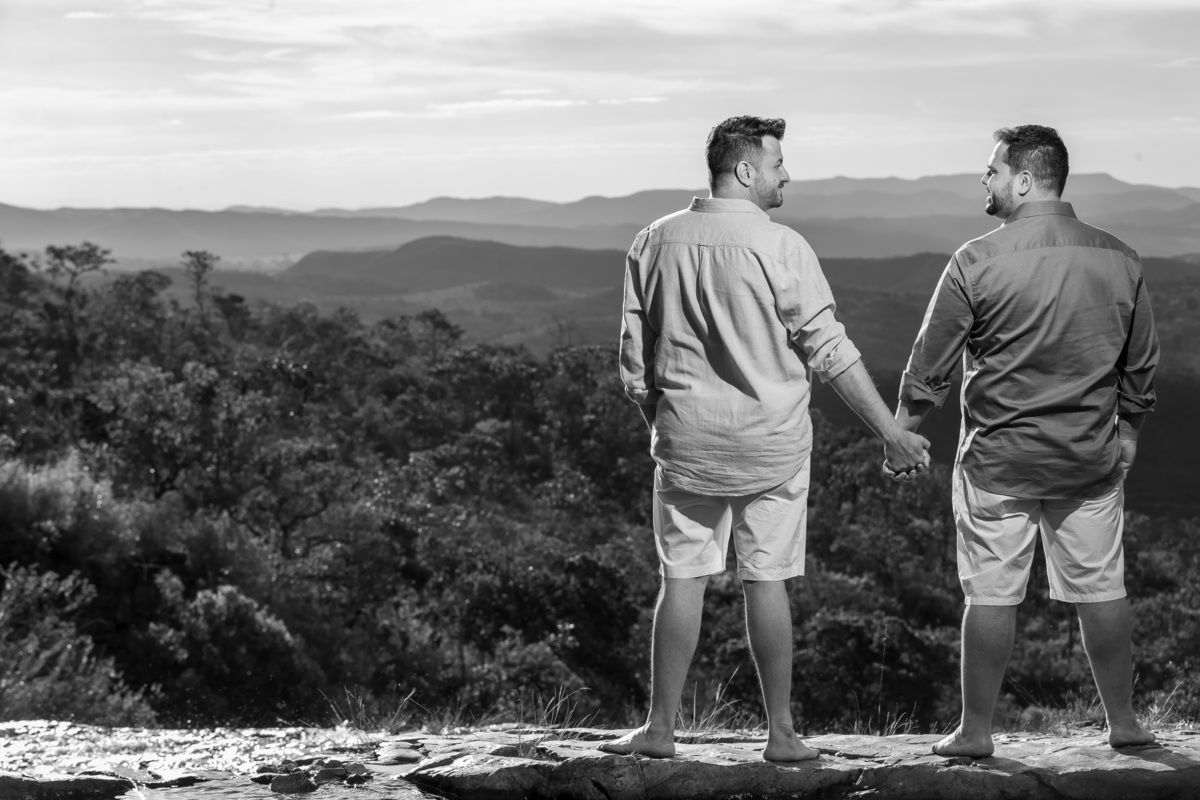 O casal está em pé, trocando olhares e sorrindo, ao fundo o horizonte do serrado em uma linda fotografia preto e branco.