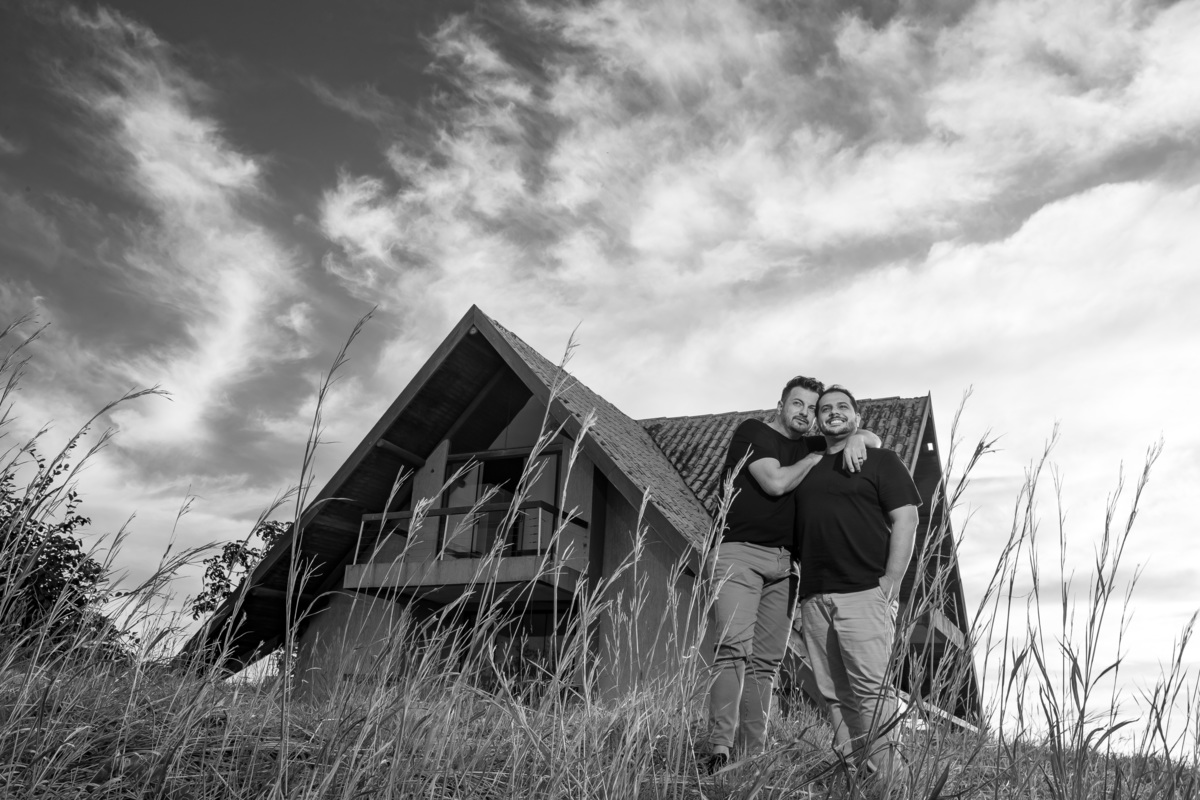 Abraçados e ao fundo a casa de hóspedes do Paraíso na Terra, o casal abraçados e vendo o horizonte, tudo em uma linda fotografia preto e branco.