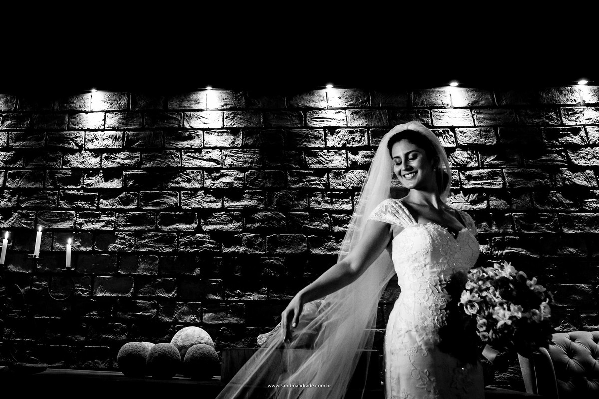 Um sorriso encantador, seu véu, o vestido e o buque magnifico, com uma bela iluminação em um preto e branco exuberante.