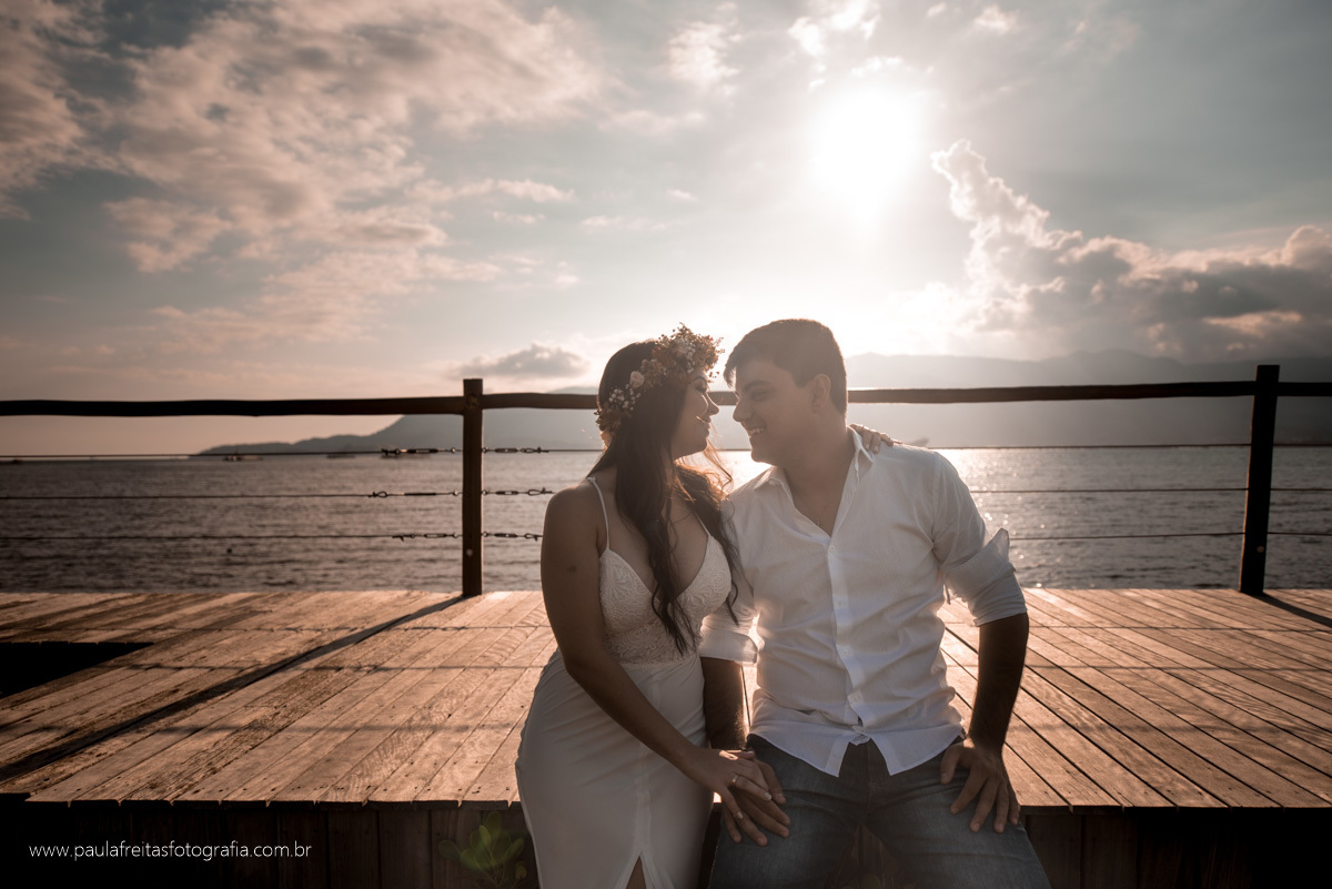 noivos sentados no dek com fundo praia e sol em ilhabela por pula freitas