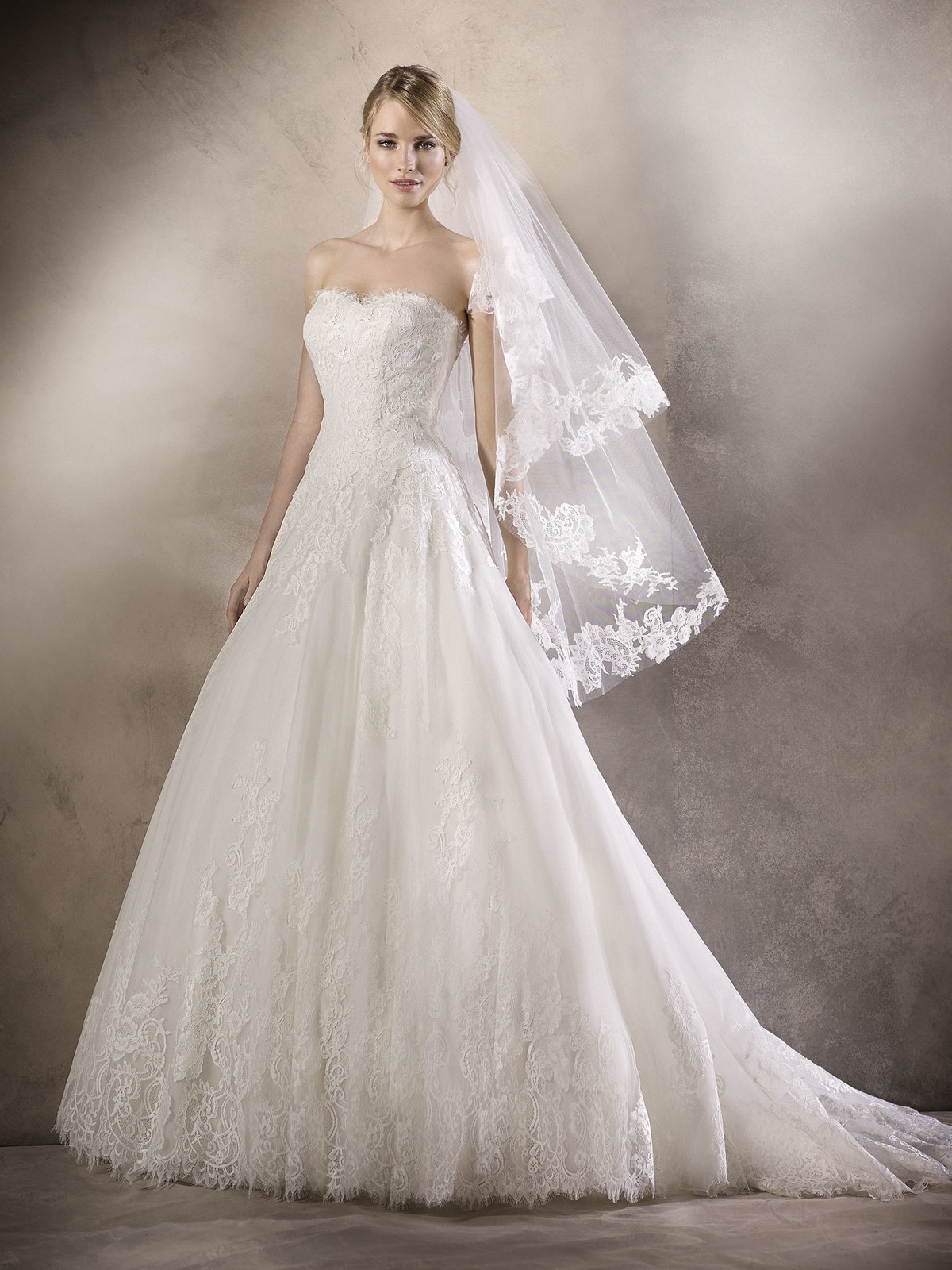 Requintado vestido de noiva estilo princesa em tule, com decote em coração. A renda decora o decote e todo o vestido, conferindo um ar muito romântico, rematado por umas costas com elegantes botões.