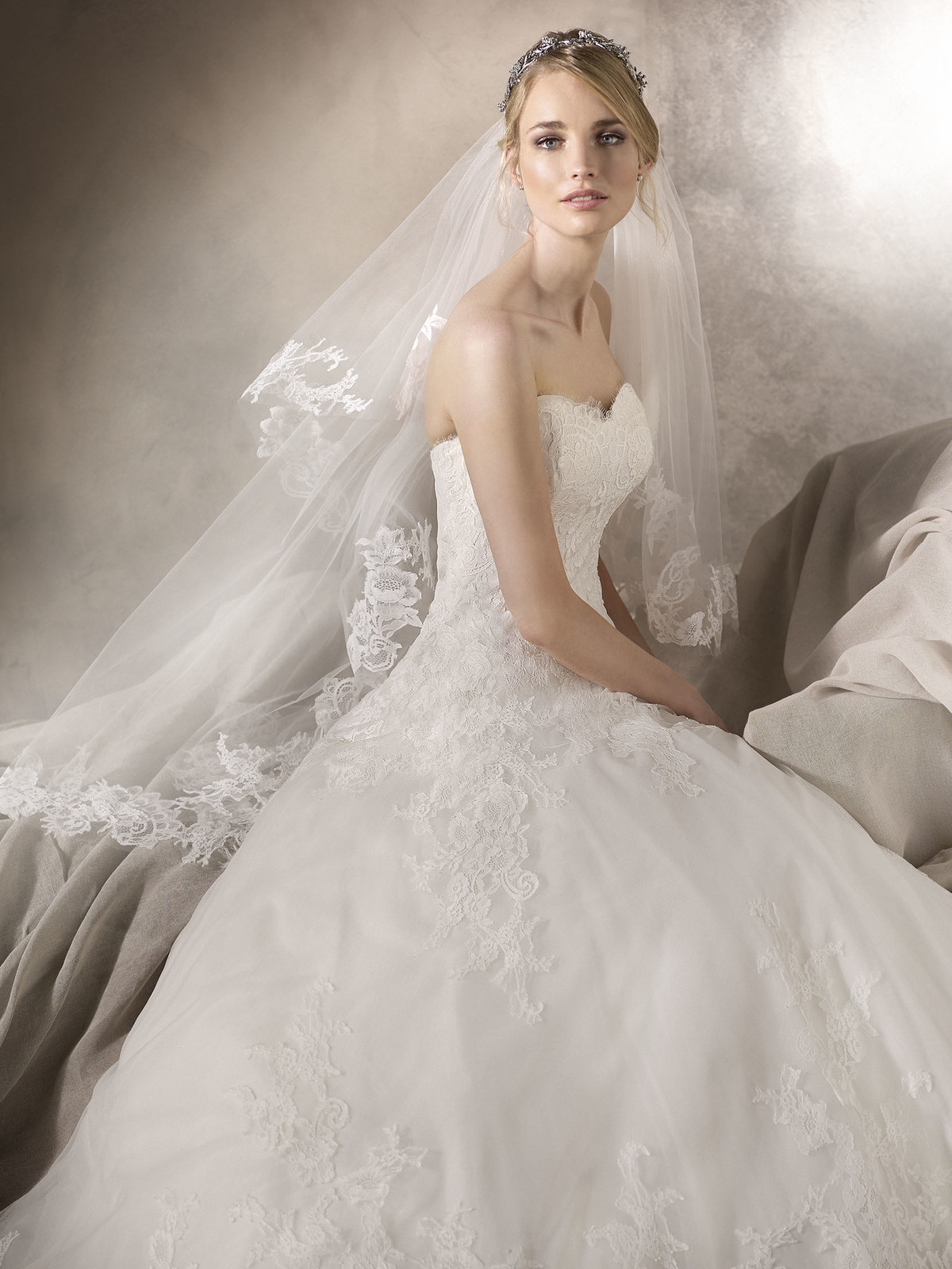 Requintado vestido de noiva estilo princesa em tule, com decote em coração. A renda decora o decote e todo o vestido, conferindo um ar muito romântico, rematado por umas costas com elegantes botões.