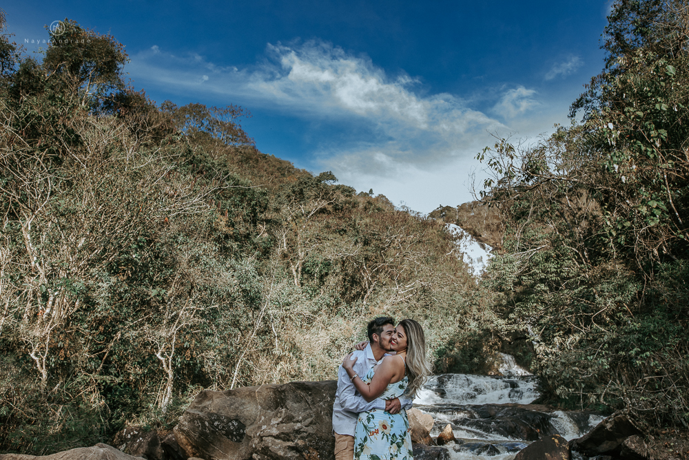 Ensaio casal pre-wedding na cachoeira com céu azul no entardecer.