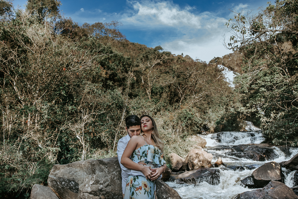 Ensaio casal pre-wedding na cachoeira com céu azul no entardecer.