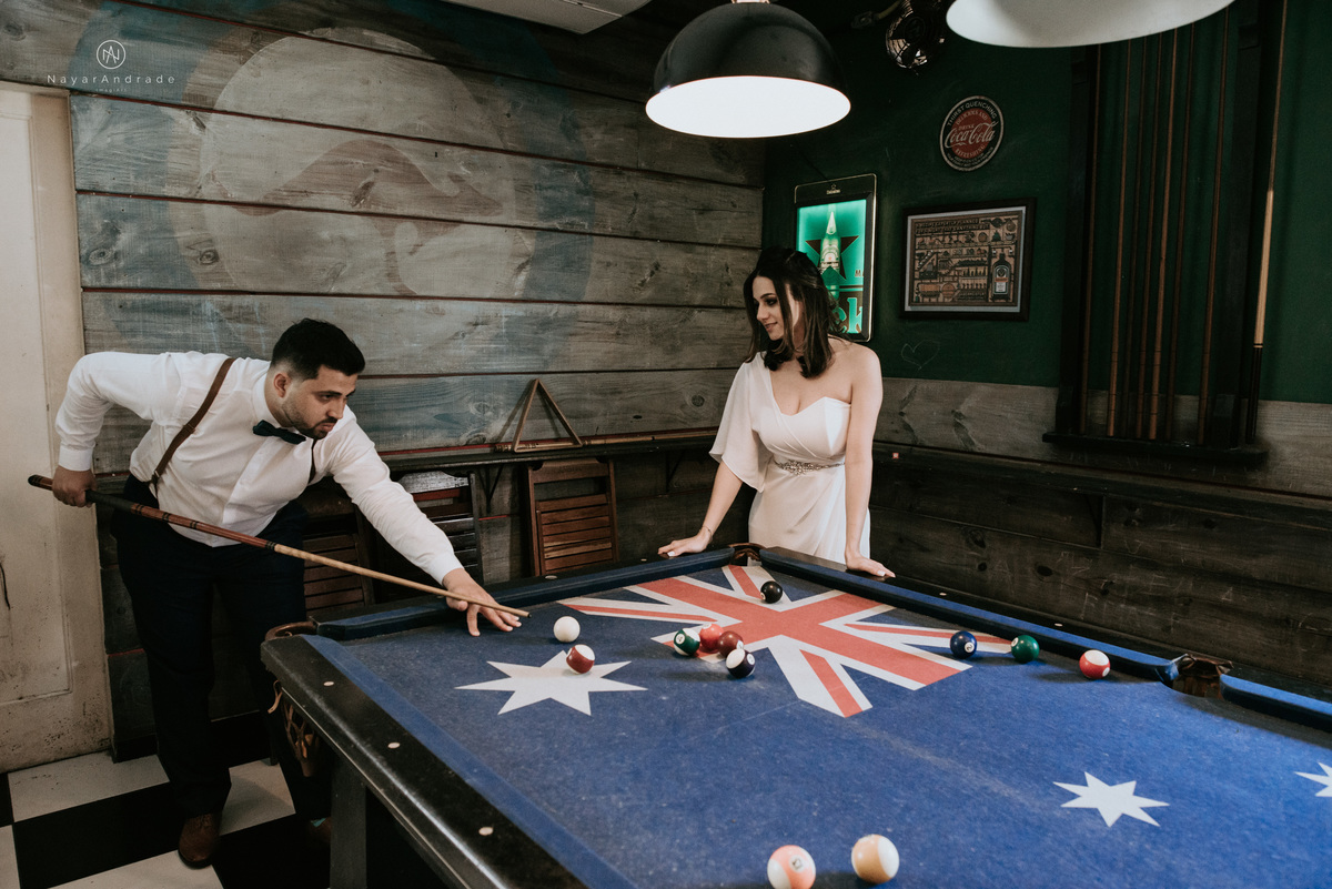 Mini wedding em Santos no australiano bar, noiva com vestido longo de fenda e noivo de suspensorio e gravata borboleta. Fotos de casamento na mesa de sinuca e no bar. Casal apaixonado em mini wedd de manha