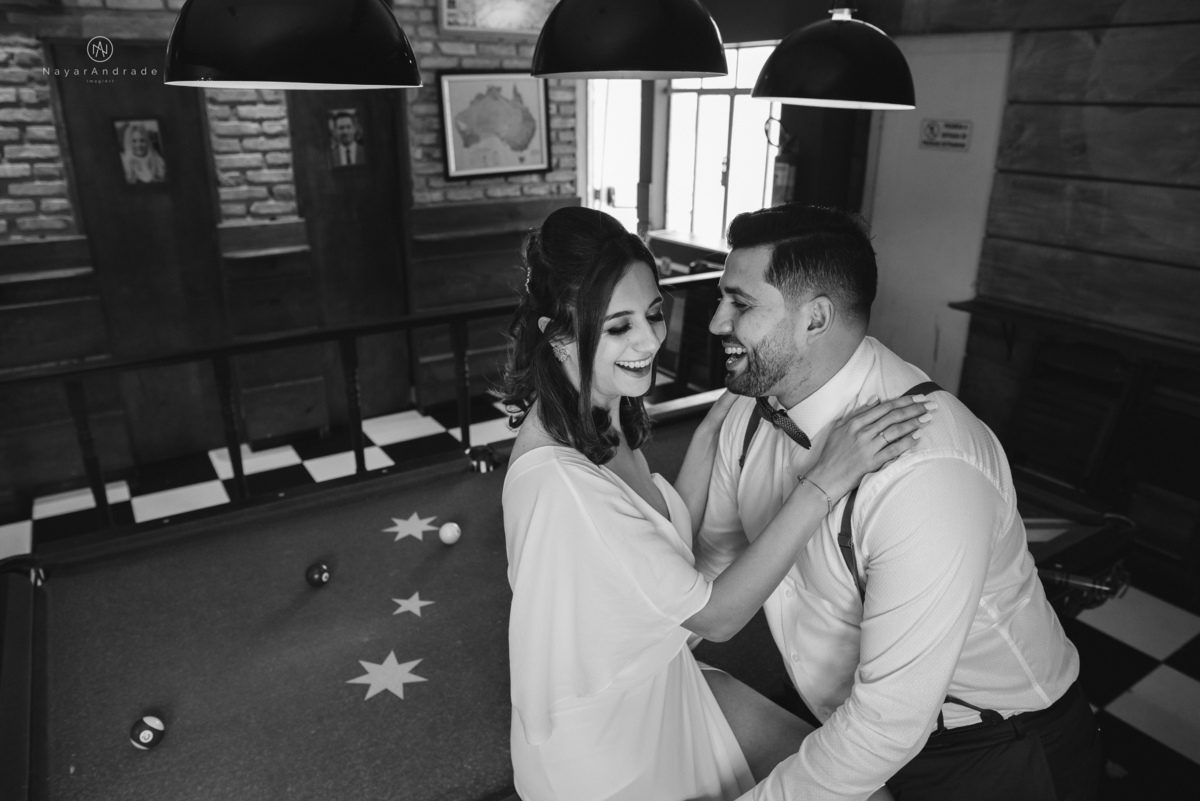 Mini wedding em Santos no australiano bar, noiva com vestido longo de fenda e noivo de suspensorio e gravata borboleta. Fotos de casamento na mesa de sinuca e no bar. Casal apaixonado em mini wedd de manha