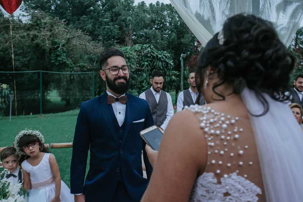 casamento ao ar livre de dia com noiva princesa e noivo de terno azul e gravata borboleta de madeira decoracao com guirlanda e padrinhos com balao de coracao