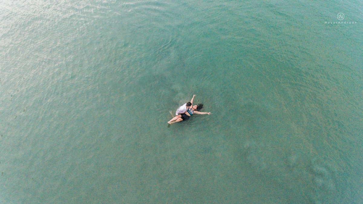 ensaio pre casamento na praia de ubatuba em sao paulo casal de blusa branca com fotos nas pedras e na agua cristalina