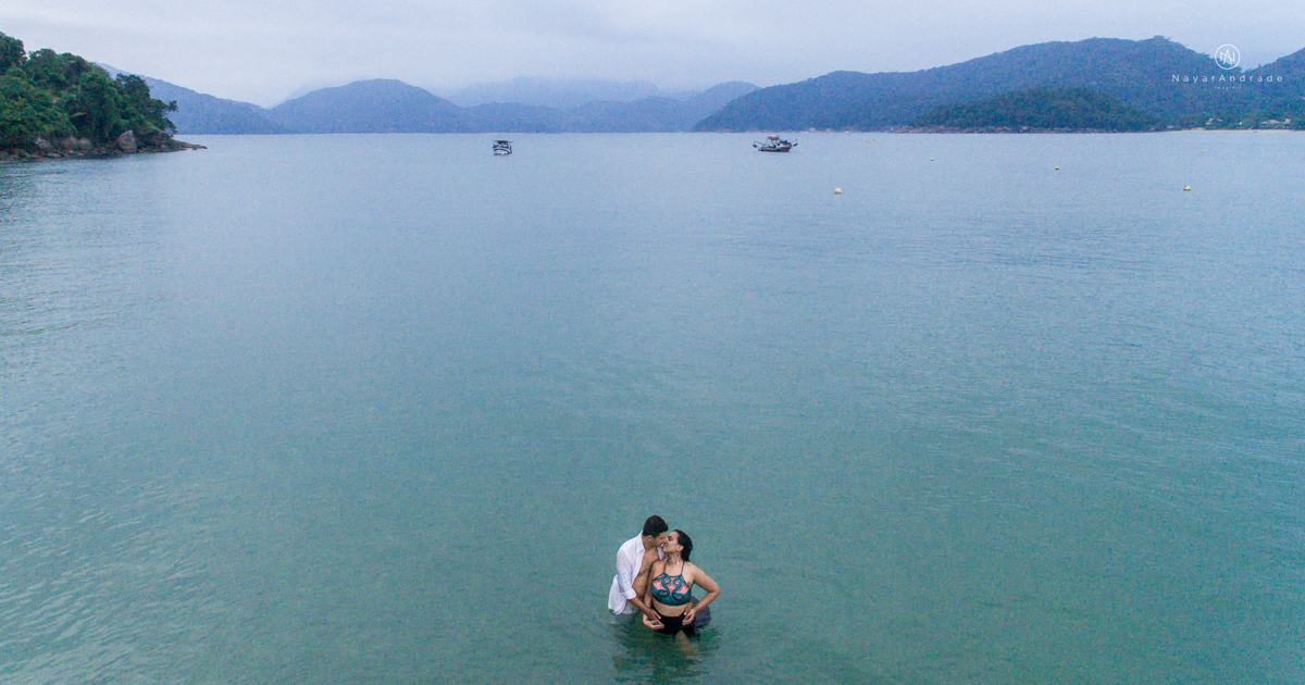 ensaio pre casamento na praia de ubatuba em sao paulo casal de blusa branca com fotos nas pedras e na agua cristalina