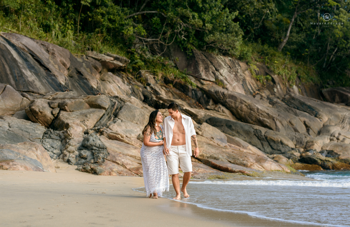 ensaio pre casamento na praia de ubatuba em sao paulo casal de blusa branca com fotos nas pedras e na agua cristalina