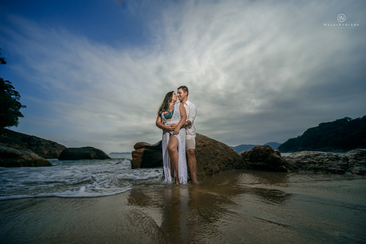 ensaio pre casamento na praia de ubatuba em sao paulo casal de blusa branca com fotos nas pedras e na agua cristalina