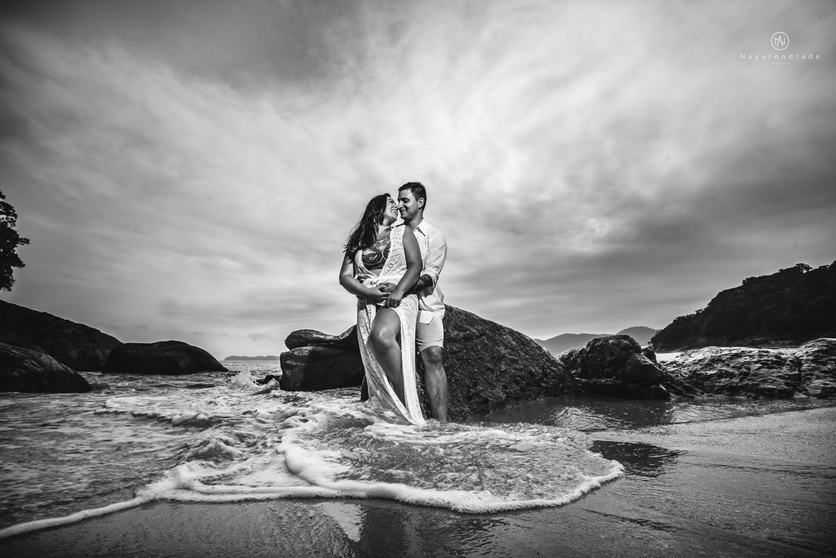 ensaio pre casamento na praia de ubatuba em sao paulo casal de blusa branca com fotos nas pedras e na agua cristalina