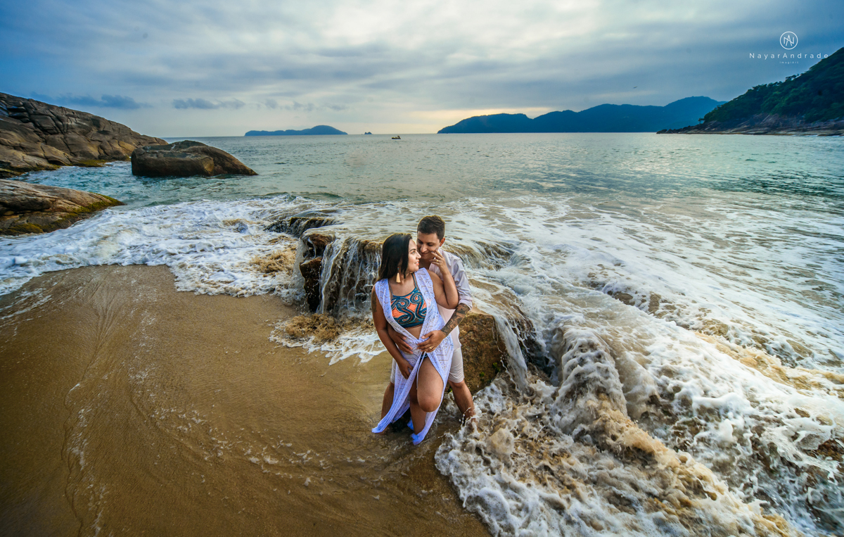 ensaio pre casamento na praia de ubatuba em sao paulo casal de blusa branca com fotos nas pedras e na agua cristalina