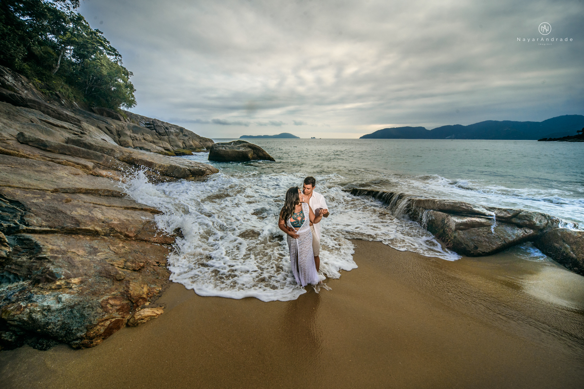 ensaio pre casamento na praia de ubatuba em sao paulo casal de blusa branca com fotos nas pedras e na agua cristalina