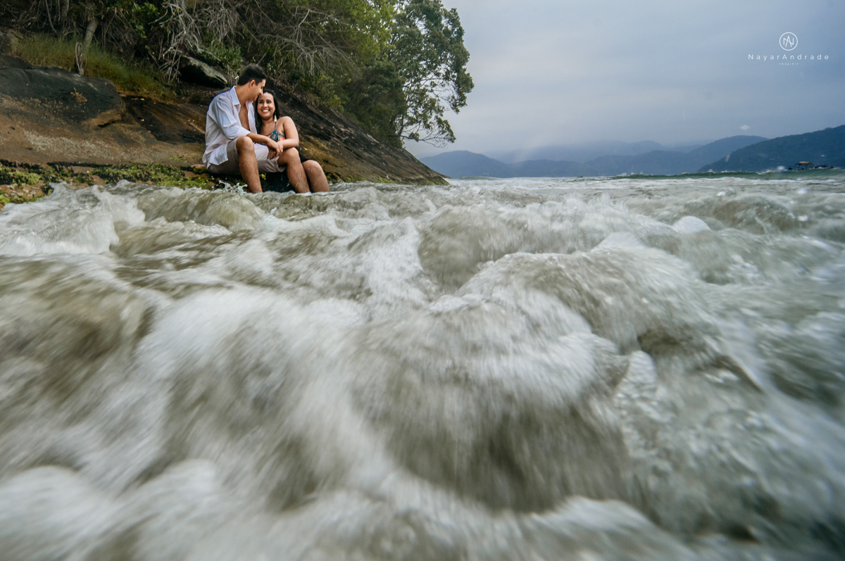 ensaio pre casamento na praia de ubatuba em sao paulo casal de blusa branca com fotos nas pedras e na agua cristalina