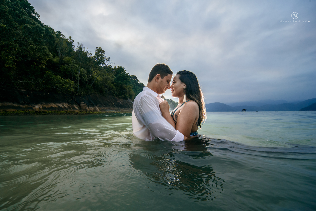 ensaio pre casamento na praia de ubatuba em sao paulo casal de blusa branca com fotos nas pedras e na agua cristalina