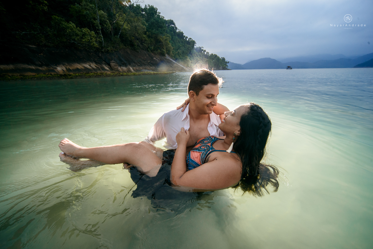 ensaio pre casamento na praia de ubatuba em sao paulo casal de blusa branca com fotos nas pedras e na agua cristalina