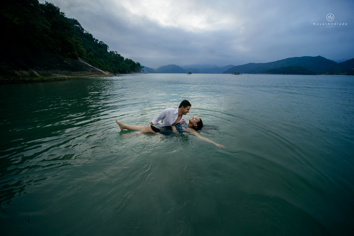 ensaio pre casamento na praia de ubatuba em sao paulo casal de blusa branca com fotos nas pedras e na agua cristalina