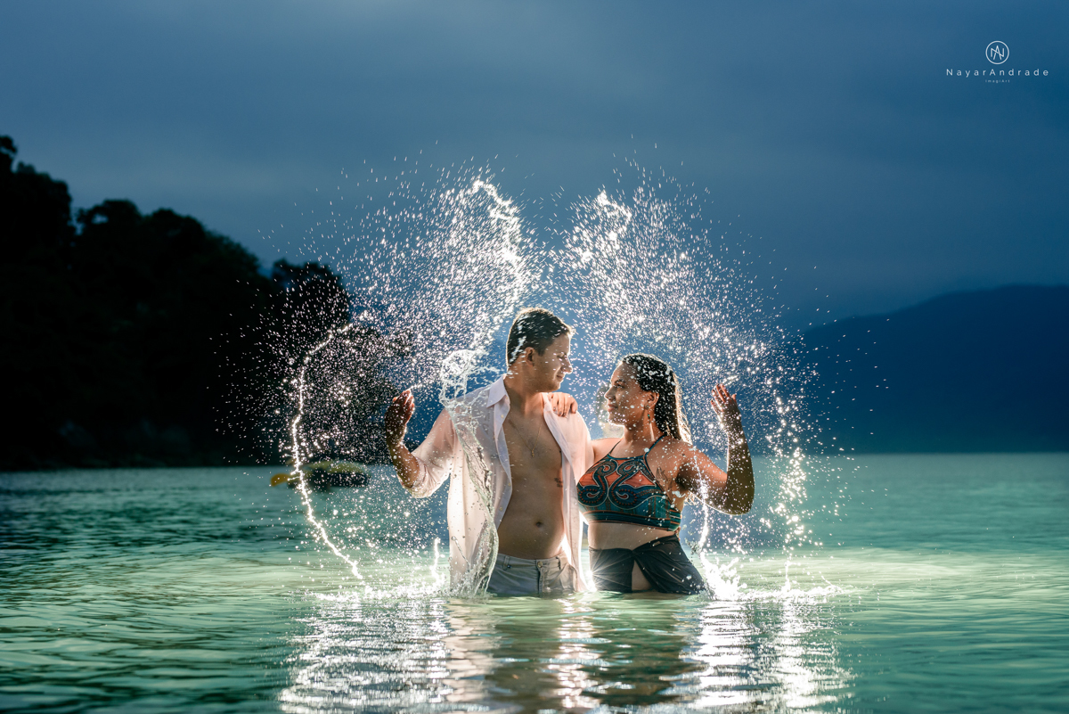 ensaio pre casamento na praia de ubatuba em sao paulo casal de blusa branca com fotos nas pedras e na agua cristalina