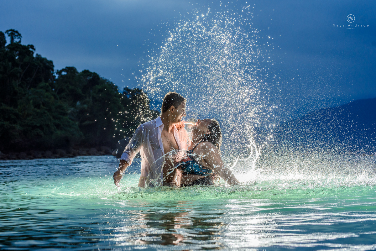 ensaio pre casamento na praia de ubatuba em sao paulo casal de blusa branca com fotos nas pedras e na agua cristalina
