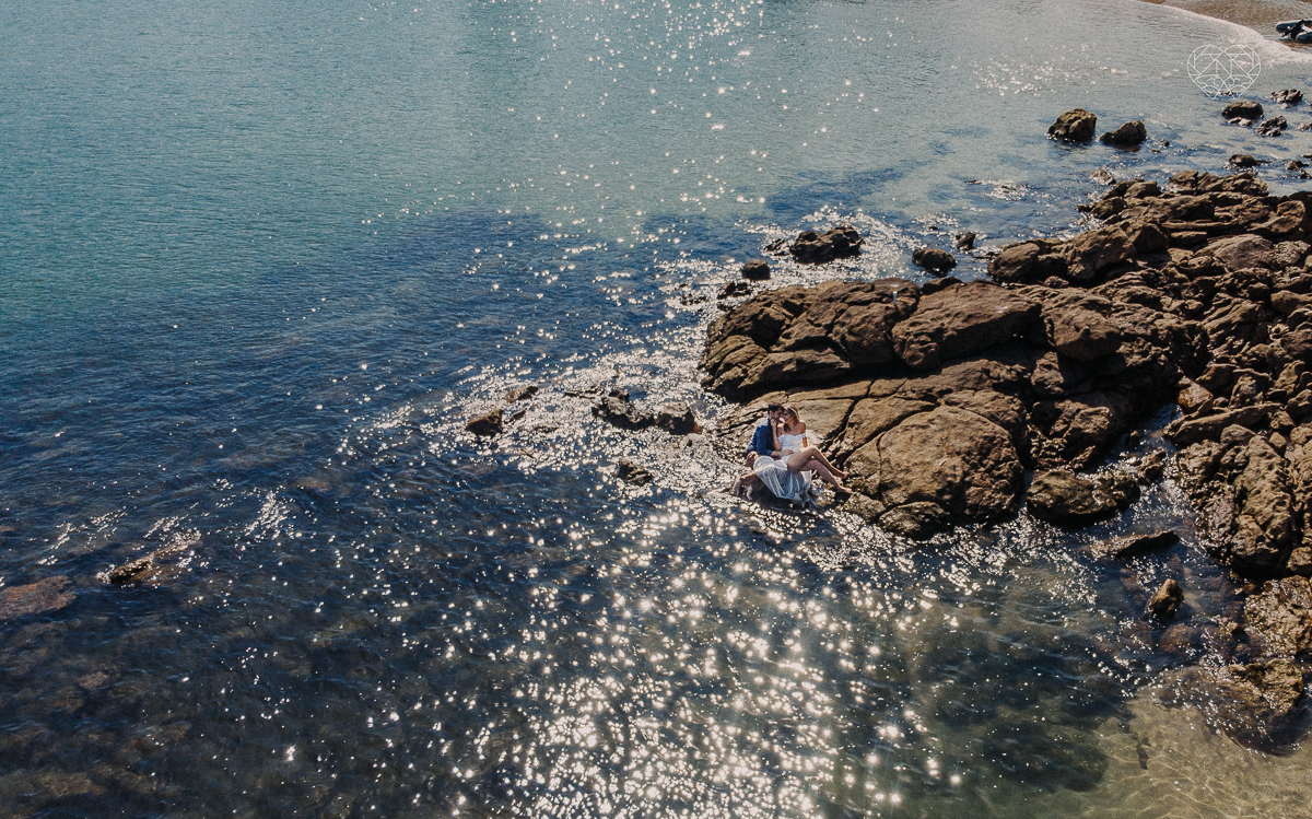 ensaio pre casamento pre wedding na praia das conchas no guaruja noiva de roupa branca e buque e noivo com roupa sociall fotos feitas na agua  na grama e correndo nas pedras ensaio feito pela fotografa premiada nayara andrade de santos