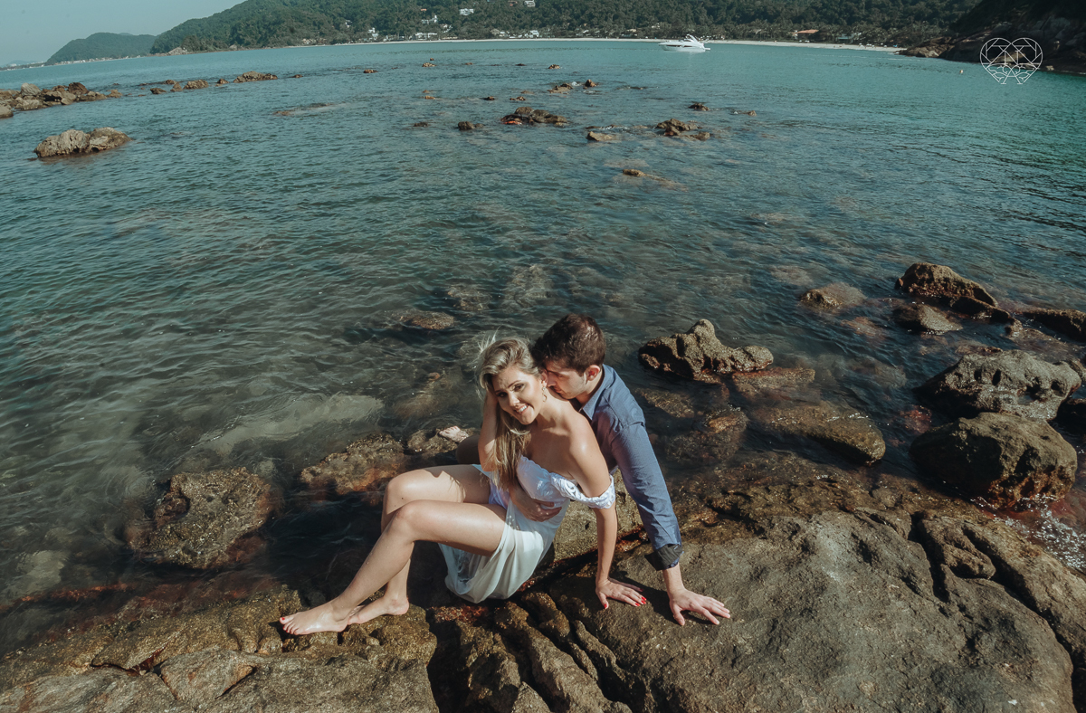 ensaio pre casamento pre wedding na praia das conchas no guaruja noiva de roupa branca e buque e noivo com roupa sociall fotos feitas na agua  na grama e correndo nas pedras ensaio feito pela fotografa premiada nayara andrade de santos