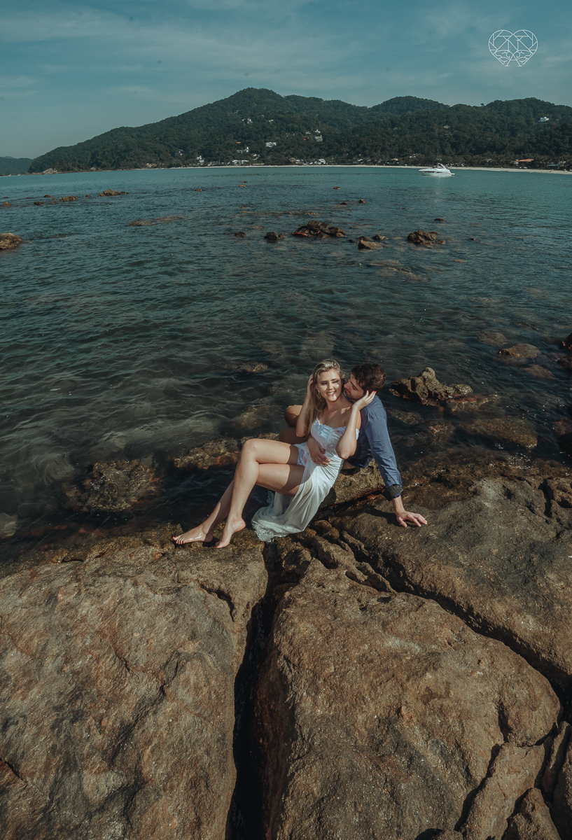 ensaio pre casamento pre wedding na praia das conchas no guaruja noiva de roupa branca e buque e noivo com roupa sociall fotos feitas na agua  na grama e correndo nas pedras ensaio feito pela fotografa premiada nayara andrade de santos