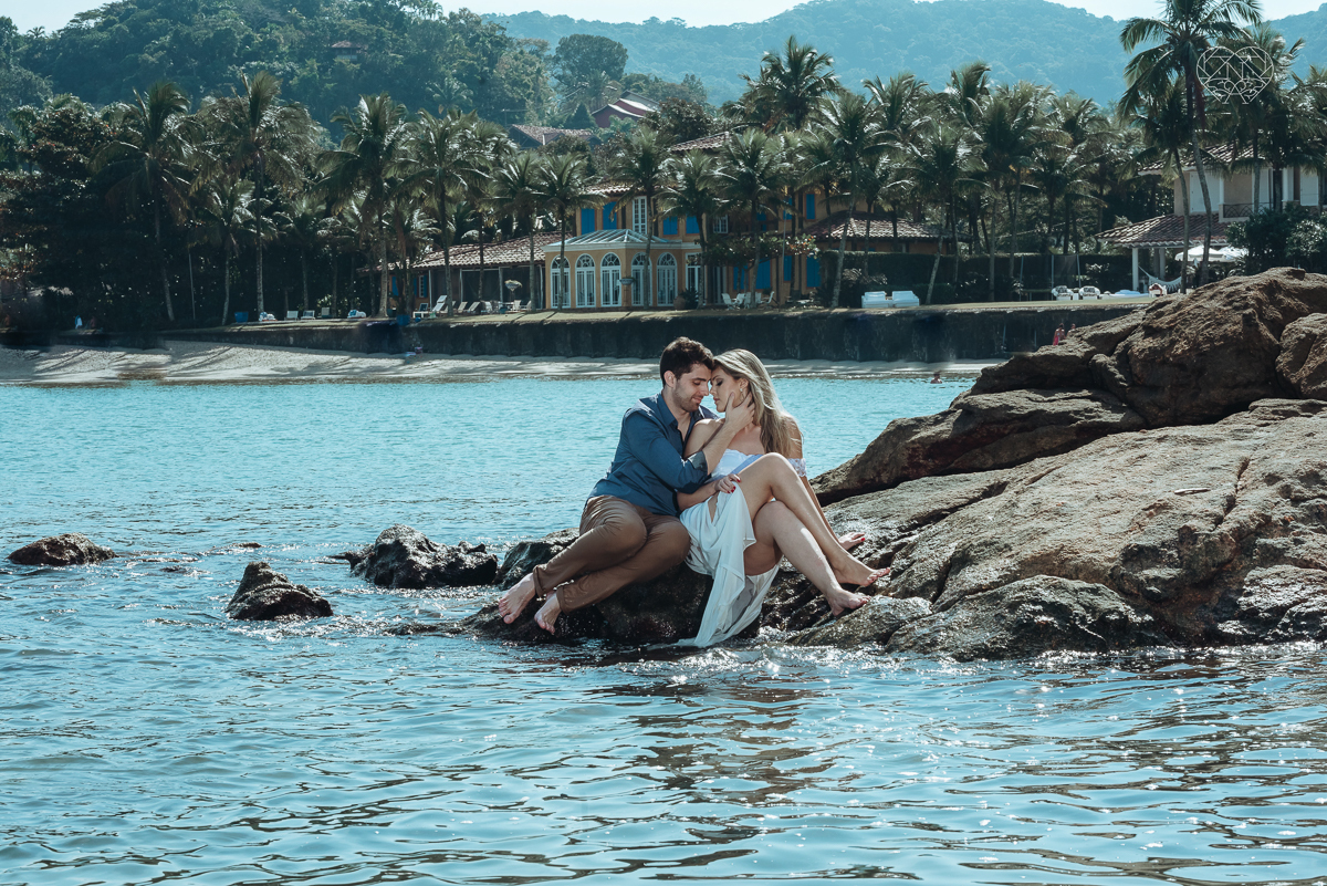 ensaio pre casamento pre wedding na praia das conchas no guaruja noiva de roupa branca e buque e noivo com roupa sociall fotos feitas na agua  na grama e correndo nas pedras ensaio feito pela fotografa premiada nayara andrade de santos