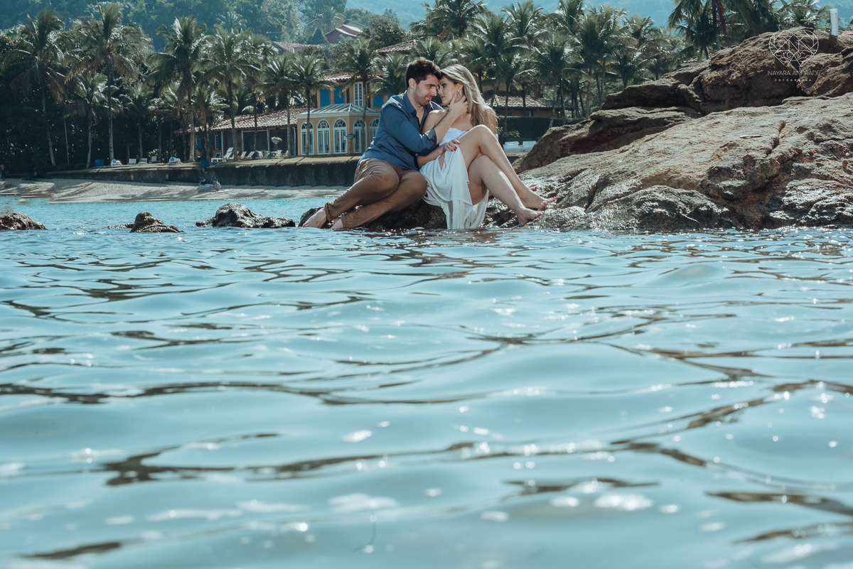 ensaio pre casamento pre wedding na praia das conchas no guaruja noiva de roupa branca e buque e noivo com roupa sociall fotos feitas na agua  na grama e correndo nas pedras ensaio feito pela fotografa premiada nayara andrade de santos