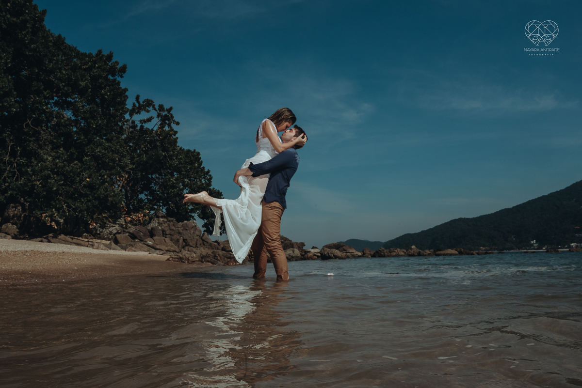 ensaio pre casamento pre wedding na praia das conchas no guaruja noiva de roupa branca e buque e noivo com roupa sociall fotos feitas na agua  na grama e correndo nas pedras ensaio feito pela fotografa premiada nayara andrade de santos