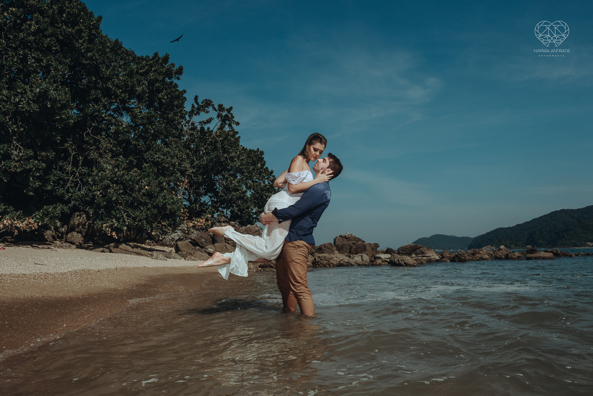 ensaio pre casamento pre wedding na praia das conchas no guaruja noiva de roupa branca e buque e noivo com roupa sociall fotos feitas na agua  na grama e correndo nas pedras ensaio feito pela fotografa premiada nayara andrade de santos