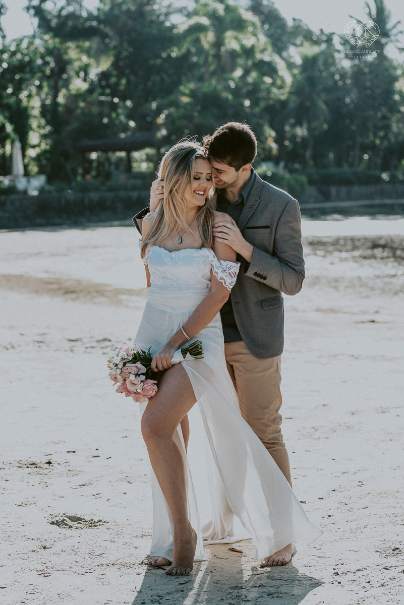 ensaio pre casamento pre wedding na praia das conchas no guaruja noiva de roupa branca e buque e noivo com roupa sociall fotos feitas na agua  na grama e correndo nas pedras ensaio feito pela fotografa premiada nayara andrade de santos
