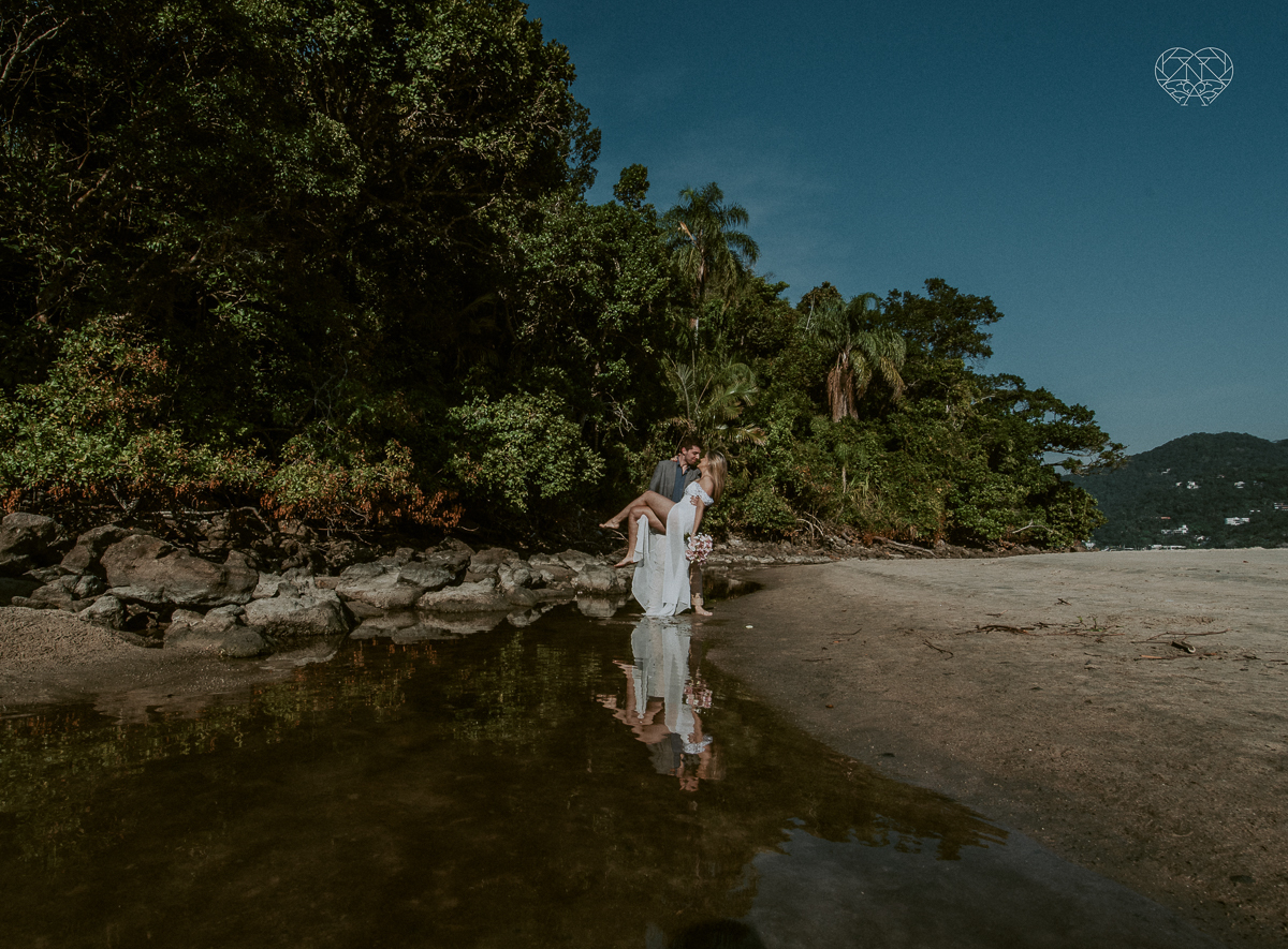 ensaio pre casamento pre wedding na praia das conchas no guaruja noiva de roupa branca e buque e noivo com roupa sociall fotos feitas na agua  na grama e correndo nas pedras ensaio feito pela fotografa premiada nayara andrade de santos