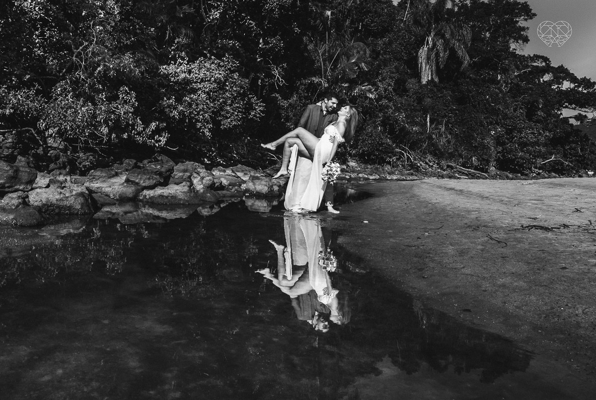 ensaio pre casamento pre wedding na praia das conchas no guaruja noiva de roupa branca e buque e noivo com roupa sociall fotos feitas na agua  na grama e correndo nas pedras ensaio feito pela fotografa premiada nayara andrade de santos