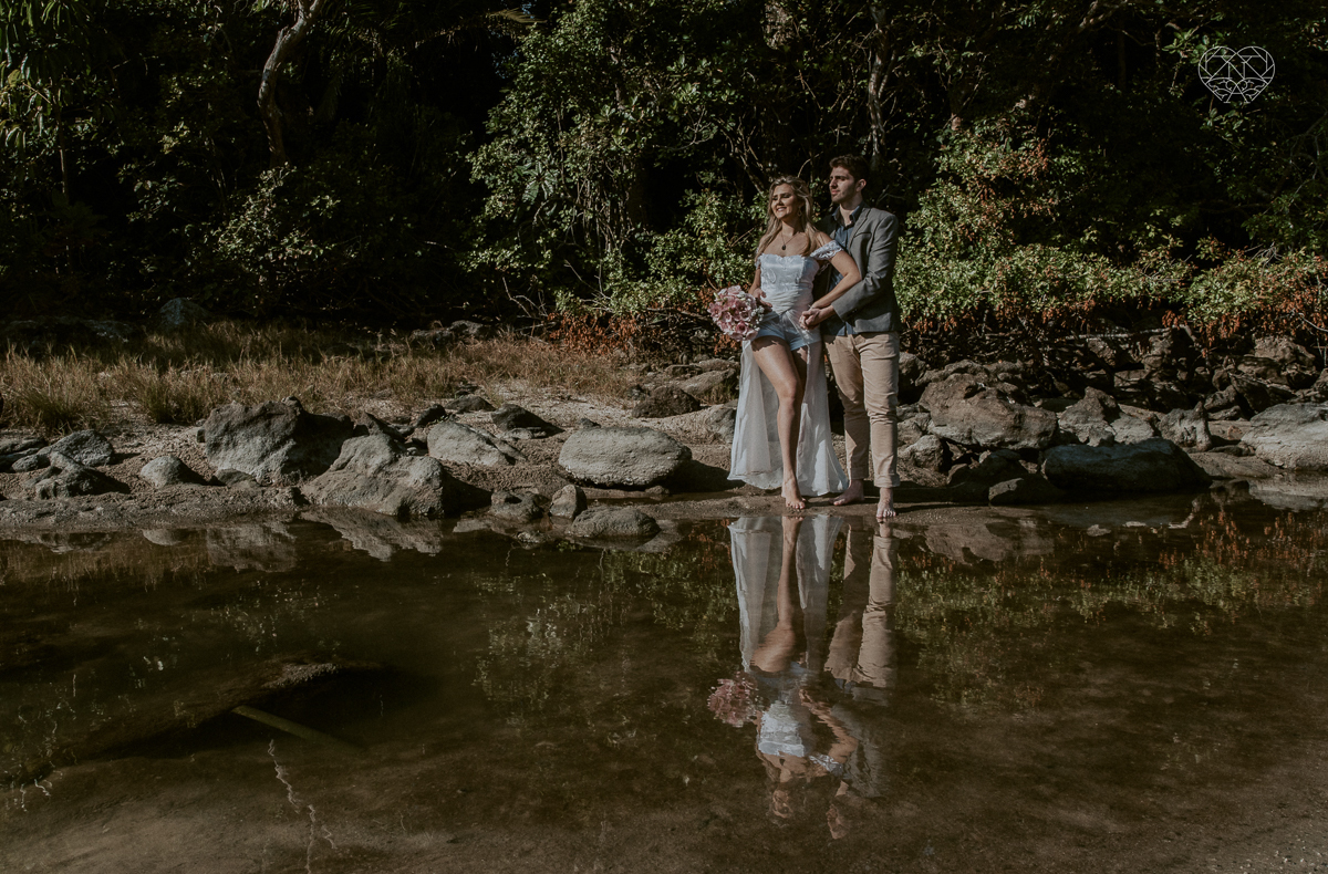 ensaio pre casamento pre wedding na praia das conchas no guaruja noiva de roupa branca e buque e noivo com roupa sociall fotos feitas na agua  na grama e correndo nas pedras ensaio feito pela fotografa premiada nayara andrade de santos