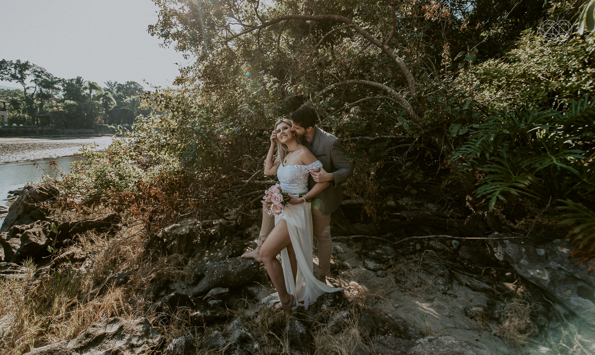 ensaio pre casamento pre wedding na praia das conchas no guaruja noiva de roupa branca e buque e noivo com roupa sociall fotos feitas na agua  na grama e correndo nas pedras ensaio feito pela fotografa premiada nayara andrade de santos