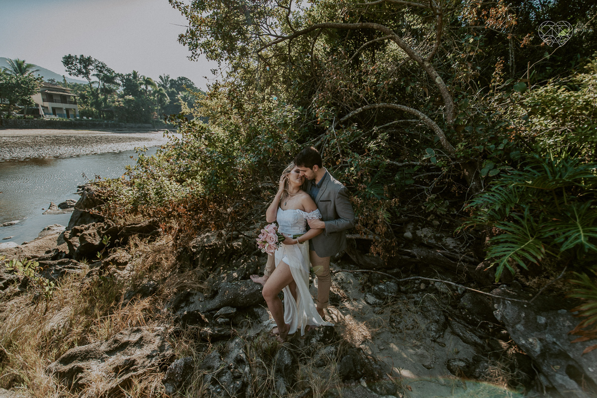 ensaio pre casamento pre wedding na praia das conchas no guaruja noiva de roupa branca e buque e noivo com roupa sociall fotos feitas na agua  na grama e correndo nas pedras ensaio feito pela fotografa premiada nayara andrade de santos