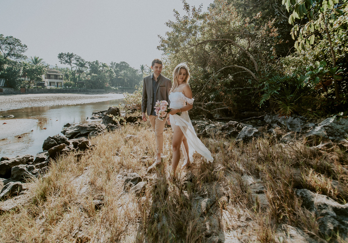 ensaio pre casamento pre wedding na praia das conchas no guaruja noiva de roupa branca e buque e noivo com roupa sociall fotos feitas na agua  na grama e correndo nas pedras ensaio feito pela fotografa premiada nayara andrade de santos